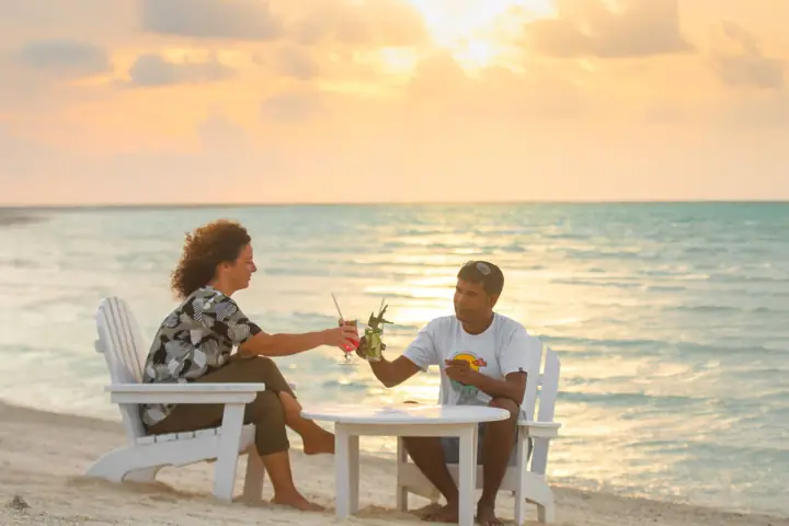 Couple enjoying drinks at a beachside table at sunset in the Maldives