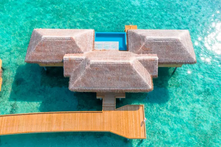 Aerial view of an overwater villa in a turquoise lagoon